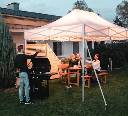 Friends celebrate a barbecue and garden party under the garden tent. The garden tent is festively decorated with fairy lights.