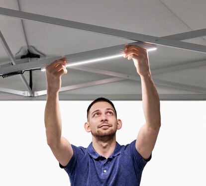 The man attaches the LED strips to the folding gazebo.